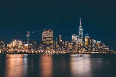 Illuminated buildings in city by river against sky at night