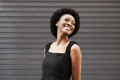 Happy afro woman wearing black dress in front of shutter