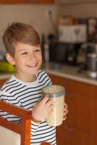 Smiling boy holding container in kitchen at home
