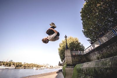 Man performing stunt by river against clear sky