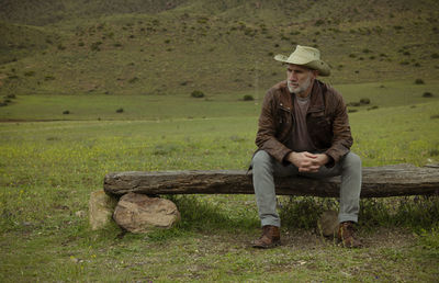 Adult man in cowboy hat sitting on wooden bench in field