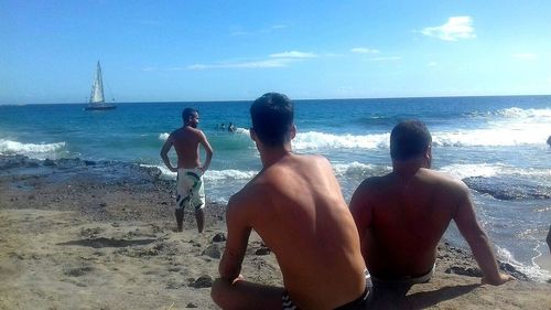 Rear view of shirtless men on beach against sky