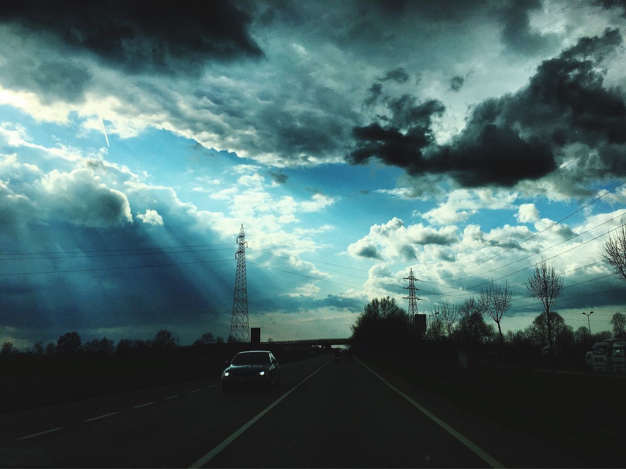 sky, transportation, road, cloud - sky, cloudy, the way forward, car, tree, electricity pylon, road marking, cloud, weather, diminishing perspective, overcast, power line, land vehicle, street, connection, nature, vanishing point