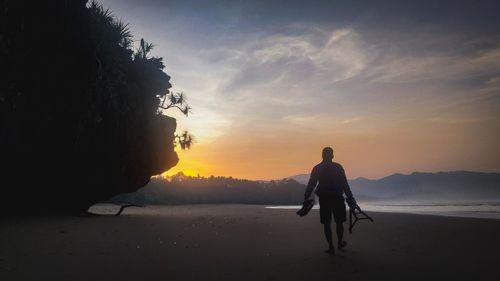 Rear view of silhouette man standing on land against sky during sunset