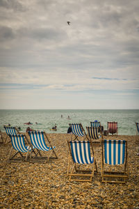 Chairs on beach against cloudy sky