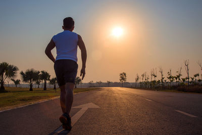 Rear view of man running on road against sky during sunset