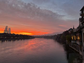 River by illuminated buildings against sky at sunset