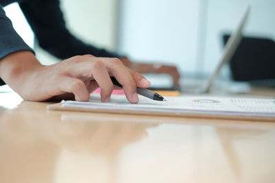 Cropped hands of businessman analyzing data at table in office 