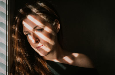 Portrait of woman looking out window with shadows across her face.