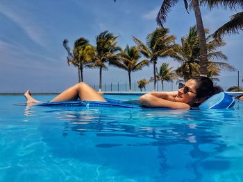 Woman relaxing in swimming pool against palm trees