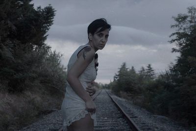 Side view of young woman standing on railroad track against sky