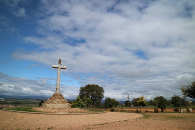 Cross on field against cloudy sky