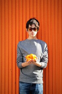 Portrait of teenage boy holding oranges while standing by wall
