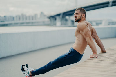 Full length of shirtless man exercising while looking away outdoors