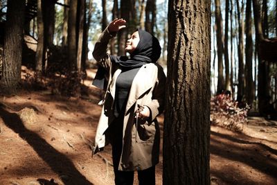 Young woman looking up while standing by tree trunk