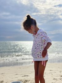 Rear view of woman standing at beach against sky