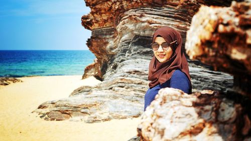 Woman on rock at beach against sky