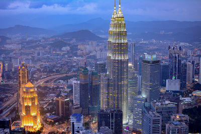 Illuminated petronas towers by buildings at dusk