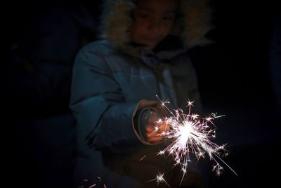 Close-up of woman in fur coat holding lit sparkler at night