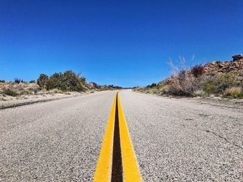 Empty country road against clear blue sky on sunny day