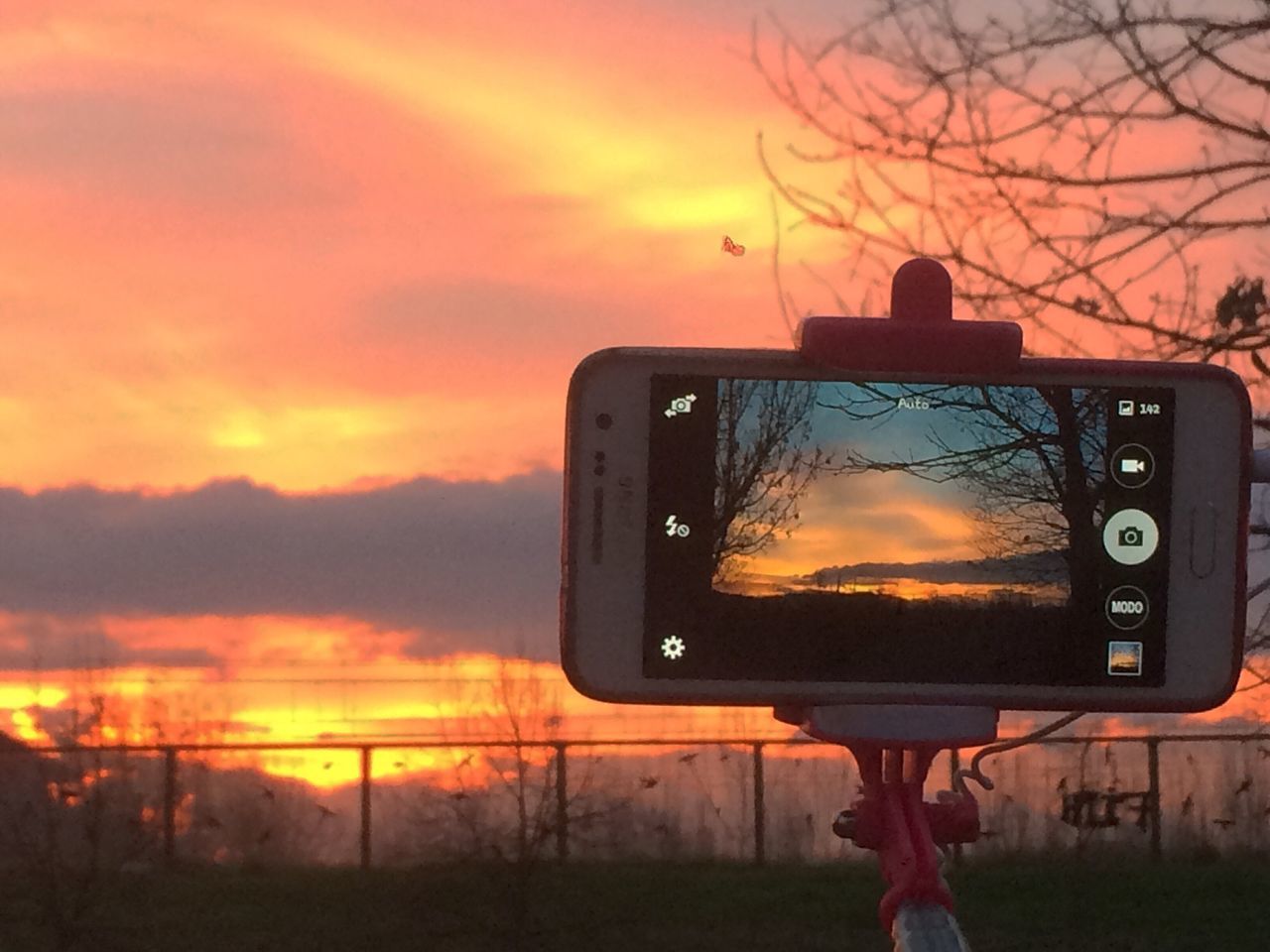 sunset, orange color, sky, communication, technology, photography themes, wireless technology, silhouette, camera - photographic equipment, photographing, field, cloud - sky, smart phone, holding, outdoors, landscape, part of, person