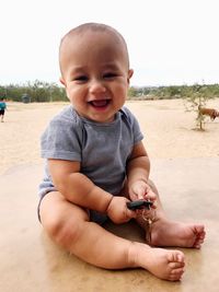 Portrait of happy boy playing with key at beach against sky