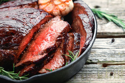 Close-up of cooked meat with rosemary and garlic in bowl on table