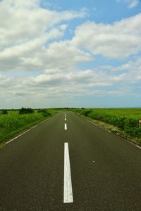 Empty road amidst field against sky