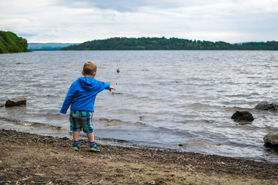 Rear view of boy throwing stone in water while standing on shore