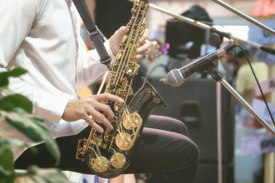 Midsection of man playing saxophone by microphone during event