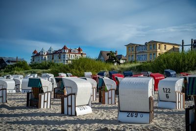 Hooded chairs on beach by buildings against sky