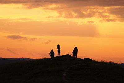 Silhouette people standing on mountain against orange sky