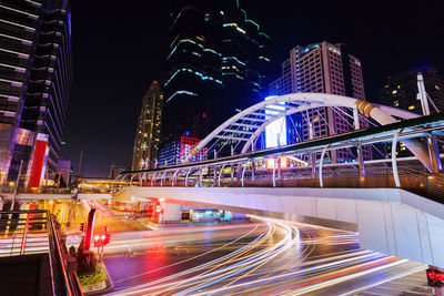 Light trails on road by illuminated buildings in city at night