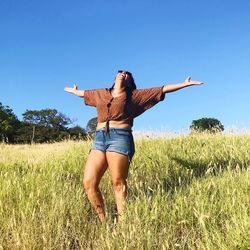 Full length of young woman with arms raised on field