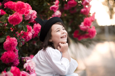 Happy kid girl 4-5 year old wearing stylish clothes posing in pink roses outdoors. summer time. 