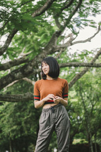 Low angle view of thoughtful young woman looking away while standing against trees in park