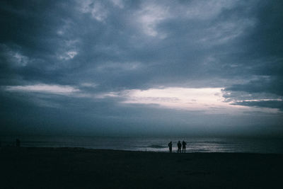 Silhouette people on beach against sky at dusk