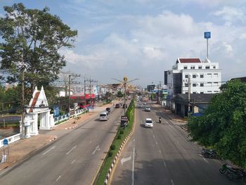 Cars on road by buildings in city against sky