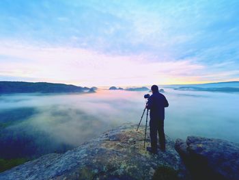 Man photographing on rock against sky