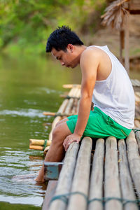 Young man sitting on wood by lake