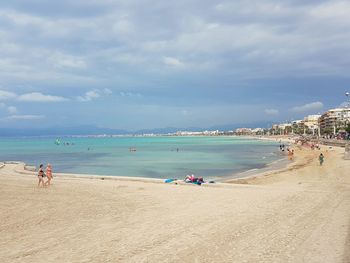 People on beach against cloudy sky