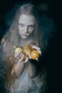 Portrait of spooky young woman with fruits against black background