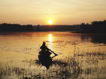 Silhouette man standing by lake against sky during sunset