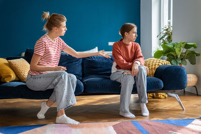 Conflict between parent and child. teenage girl sits on couch facing away from toxic mother