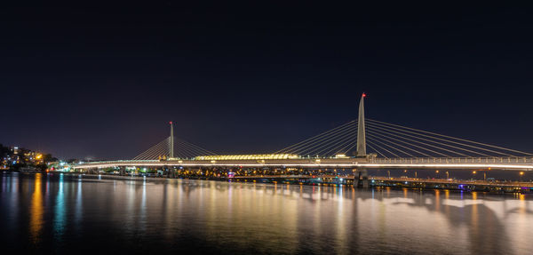Illuminated bridge over river against sky at night