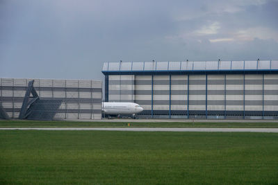 Airplane on runway in front of warehouse against sky