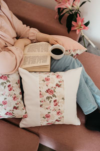 Low section of woman reading book sitting on sofa at home