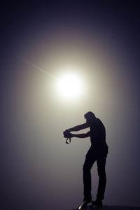 Silhouette man standing against illuminated lamp