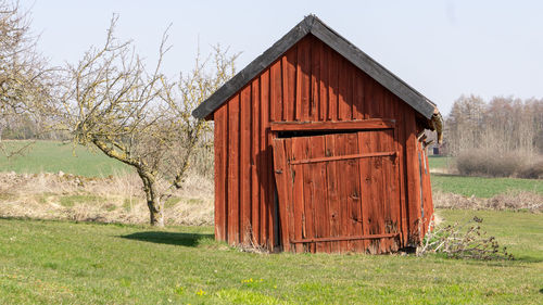 Old barn on field by house against sky