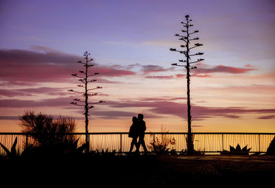 Silhouette men standing by railing against sky during sunset